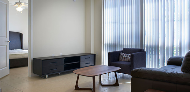 Furnished living room with hard surface flooring, windows with vertical blinds, and views into the adjacent bedroom.